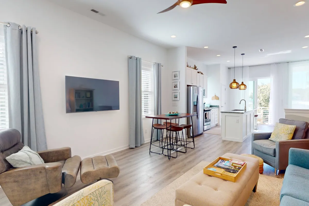 A cozy and modern open-plan interior featuring a comfortable seating area, a dining table for group meals, a kitchen island for food preparation or socializing, and large windows that flood the space with natural light. The scene captures people relaxing with family, entertaining guests, cooking, and enjoying meals together.