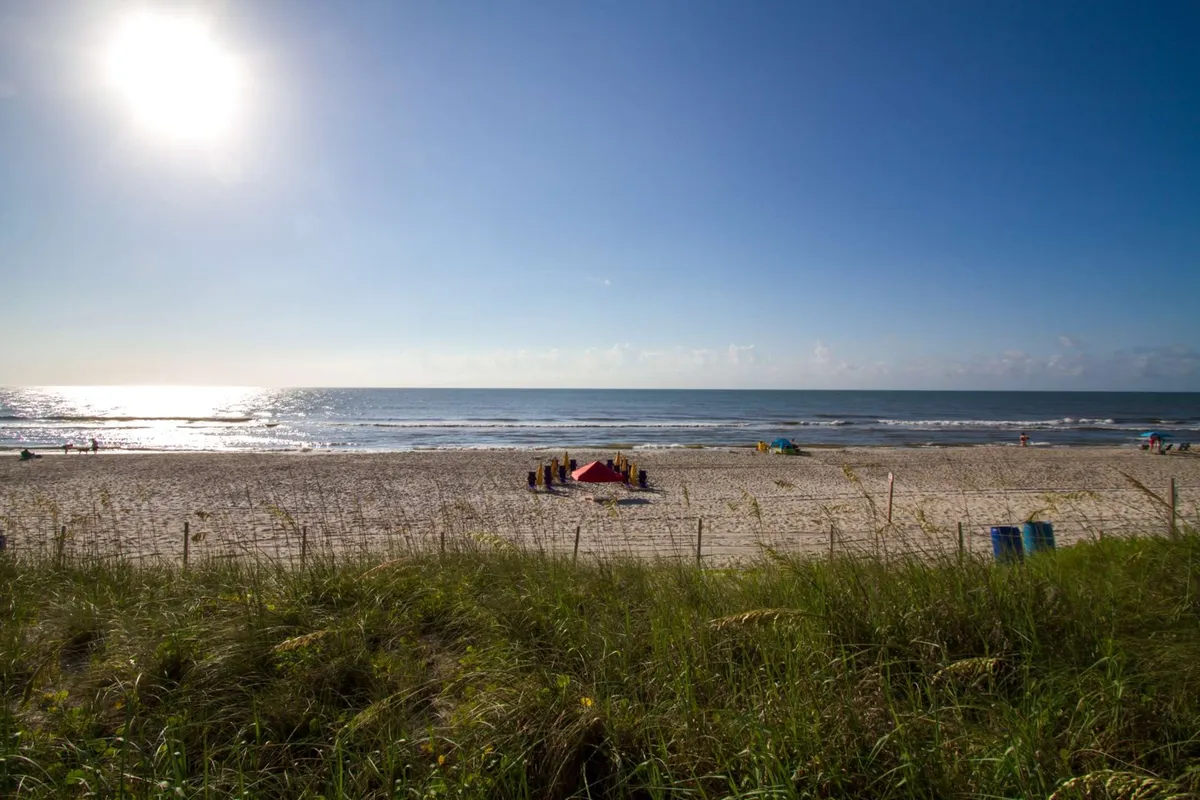 A joyful beach scene with families and children playing in the sand, swimming, and enjoying a sunny day by the ocean. The image exudes a carefree and energetic mood, emphasizing fun and togetherness on the shoreline.