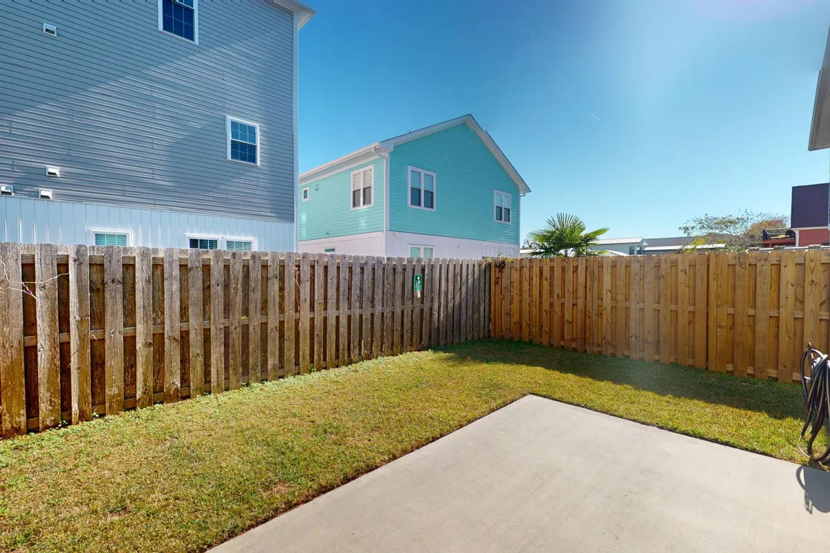A relaxed backyard scene with lush green grass, a wooden fence, and colorful houses, providing a safe and inviting space for outdoor gatherings or letting pets roam. The yard offers a sense of privacy and tranquility, suitable for both pets and their owners.