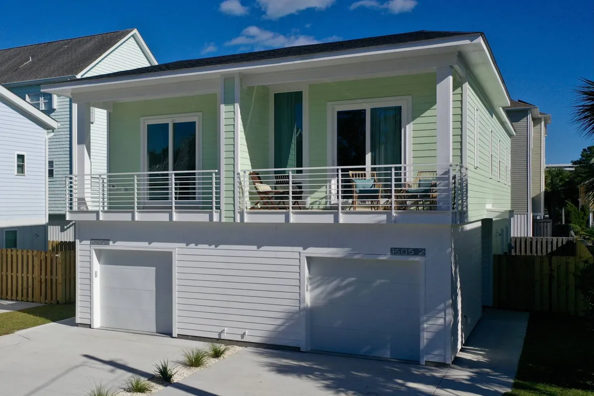 This image highlights the exterior of the home with a prominent second-story balcony featuring outdoor seating. Large windows and a green exterior create an inviting, cheerful vibe, while the attached garage and driveway are visible in the foreground.