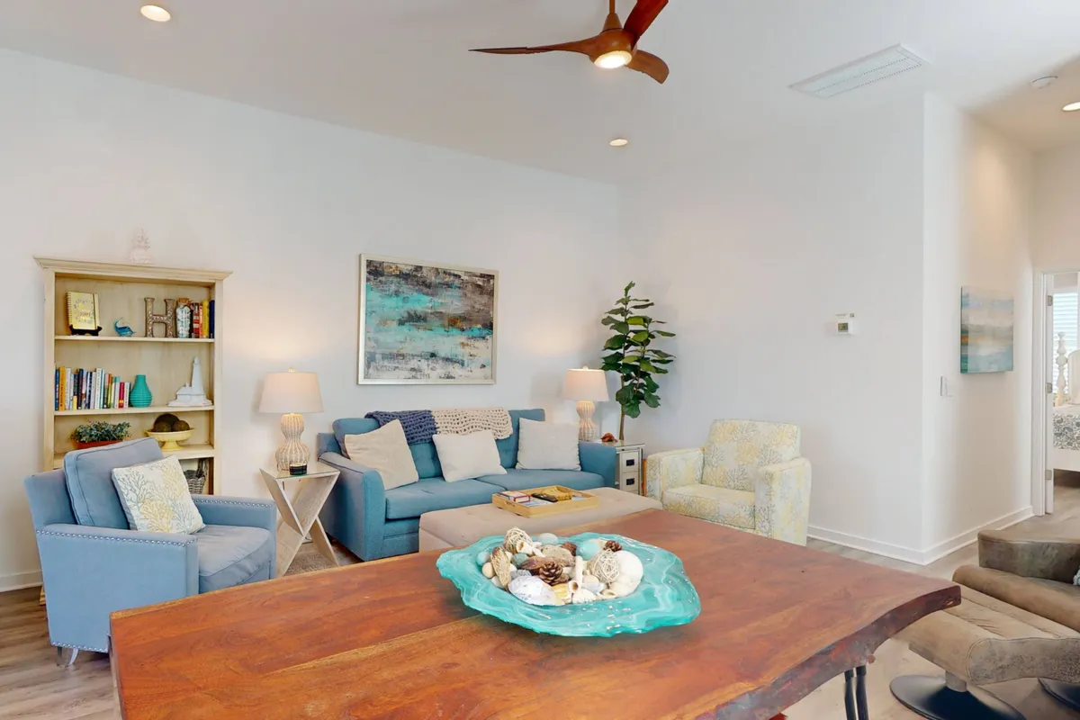 A welcoming interior shot that highlights a wooden dining table with a decorative centerpiece flanked by plush blue sofas and tasteful artwork. The scene suggests a comfortable environment for gathering, sharing stories over meals, and relaxing after a day at the beach.
